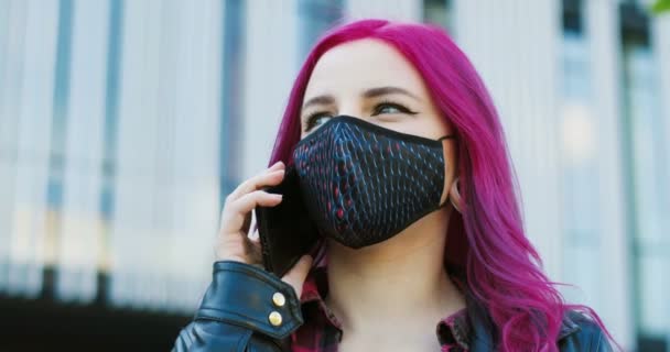 Närbild av unga kaukasiska extraordinära flicka med rosa hår och i mask stående utomhus och prata på mobiltelefon. Snygg kvinnlig hipster som talar i mobiltelefon. Ring per telefon på gatan. — Stockvideo