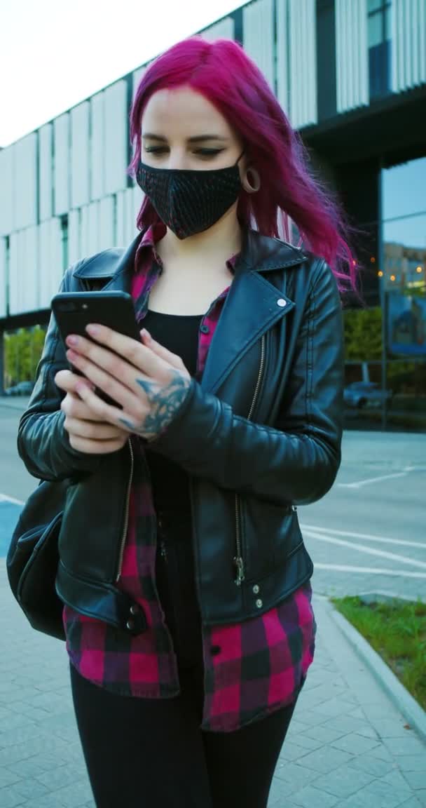 Garota extraordinária caucasiana com cabelo rosa e em pé máscara ao ar livre e mensagem de texto no smartphone. Elegante feminino hipster rolagem e tocando no telefone móvel. Orientação vertical para a história — Vídeo de Stock