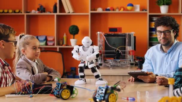 Férfi tanár elmagyarázza a gyerekeknek, hogyan kell játszani a robotokkal táblagép használatával az osztályteremben. — Stock videók