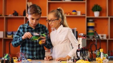 Robot makinede ustalaşan çocuk ve kız, rahat oyun odasının atmosferinde kameranın önünde onu izliyorlar.