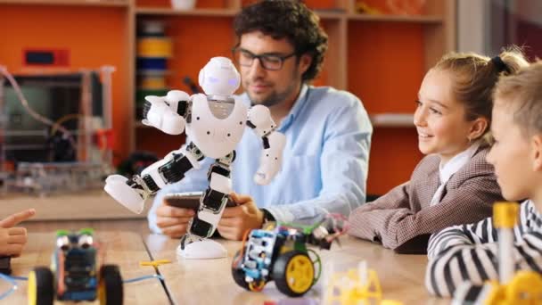 Professeur masculin avec des enfants jouant avec le robot à l'aide de la tablette dans la salle de jeu moderne à la leçon. Intérieur — Video