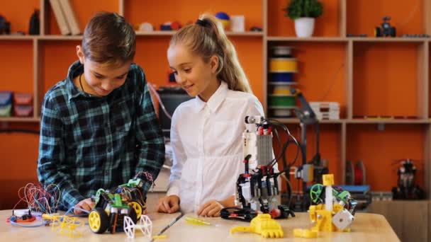Κορίτσι και αγόρι παίζει με ρομπότ και μηχανές μπροστά από την κάμερα στην ωραία ατμόσφαιρα παιχνιδιού της άνετης τάξης. Πορτρέτο — Αρχείο Βίντεο