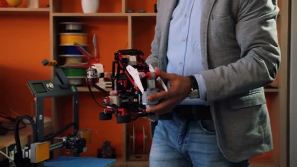 Profesor masculino tomando un robot lego de un estante y llevándolo a la mesa de los alumnos en el aula moderna. Los niños están emocionados con este juguete . — Vídeo de stock