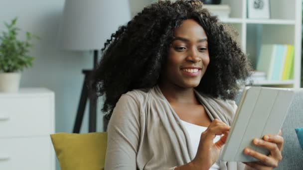 かなりアフリカ系アメリカ人の若い女性が白いタブレットPCをスクロールして夢を見ている。屋内だ。肖像画撮影 — ストック動画