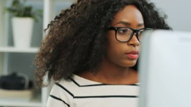 Ofisteki dizüstü bilgisayarda çalışan, gözlüklü, kıvırcık saçlı, güzel, Afro-Amerikan kadını yakından çek. Portre fotoğrafı. Kapalı