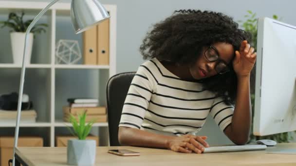 若いアフリカ系アメリカ人の女性をオフィスのコンピュータで働いているメガネで疲れさせ、休みを取ろうとしている. — ストック動画