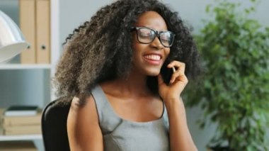 Gözlüklü güzel Afro-Amerikan kadının ofiste akıllı telefonuyla konuştuğu yakın plan. Portre çekimi.
