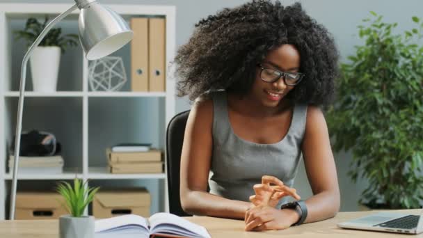 Jolie jeune femme afro-américaine en lunettes et style décontracté défilant et tapotant sur sa montre intelligente dans le bureau — Video