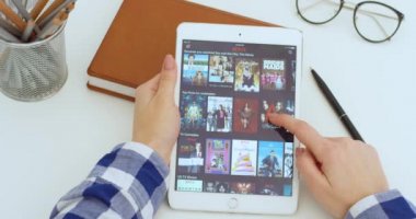New York - 15 Mayıs 2020: Beyaz tablet cihazı Netflix uygulamasını kullanan ve izlemek için film ya da dizi seçen Kafkasyalı kadının elinde. Kadın bilgisayarda tıkırdıyor ve kayıyor. Film izleme konsepti.