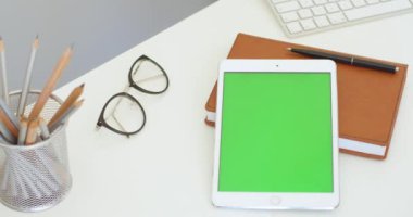Ofisteki masasında yeşil ekranlı beyaz tablet cihazını kapat. Tablet bilgisayarı, gözlük, planlayıcı ve kalemlerde krom anahtarla dikey olarak masada yatar.