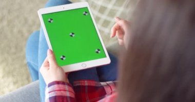 Kafkasyalı kadının elindeki beyaz tablet cihazına karşı omuz üstünden bak. Kadının elinde yeşil ekranlı bir bilgisayar var. Krom anahtar. Tıklama, yakınlaşma, takip hareketleriyle kaydırma.