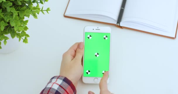 白色垂直智能手机，绿色屏幕在白人妇女手中。采用开放式规划器的白桌垂直跟踪运动的女性滚动和点击手机彩色键屏幕. — 图库视频影像
