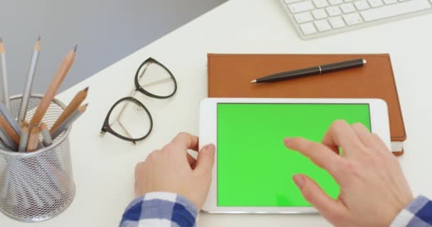 Tablette horizontale blanche avec écran vert dans les mains de la femme blanche à la table. Fille défilement, zoom et tapotement sur l'écran chromatique clé horizontalement à l'ordinateur au bureau. Navigation en ligne. — Video