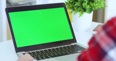 Laptop bilgisayarının üstünden yeşil ekranlı görünüyor. Krom anahtar. Beyaz bir kadın klavyede tıklıyor ve daktilo kullanıyor. Evde online çalışan serbest çalışan bir kadın..