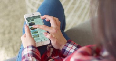 New York - 15 Mayıs 2020: Youtube uygulamasında seyahat videosu izleyen Kafkasyalı kadının ellerinde akıllı telefondan omuz üstünden görüntüleme. Kadın telefon dinlemesi ve kaydırma yapıyor. Seyahat konsepti.