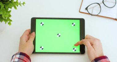 Kafkasyalı kadının ellerinde yeşil ekranlı yatay tablet bilgisayar. Kadın kaydırıyor, yakınlaştırıyor ve masadaki hareketli siyah cihazın krom anahtar ekranına vuruyor. Çevrimiçi tarama.