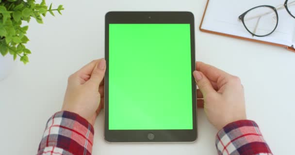 Primer plano del dispositivo de tableta negro vertical en la mesa en manos femeninas con pantalla verde. Clave de croma. Mujer viendo vídeo en la tableta en el escritorio blanco con planificador abierto . — Vídeos de Stock