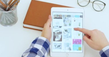New York - 15 Mayıs 2020: Beyaz tablet cihazı Pinterest uygulamasını kullanan ve ofis dekorunun fotoğraflarına bakan beyaz kadının ellerinde. Kadın bilgisayarda tıkırdıyor ve kayıyor. Tasarım konsepti.