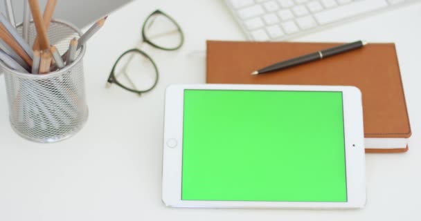 Gros plan de tablette horizontale blanche avec écran vert sur le bureau avec des trucs. Tablette couchée sur la table avec clé chromatique aux lunettes, planificateur et stylos. — Video