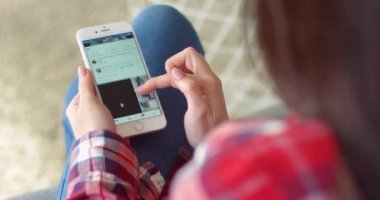 New York - 15 Mayıs 2020: FB uygulaması kullanan beyaz bir kadının ellerinde akıllı telefondan omuz üstünden görüntüleme. Telefondaki Facebook uygulamasında kadın tıklama, yakınlaştırma ve kaydırma haber sayfası.