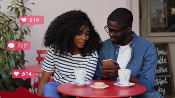 Joven pareja afroamericana sentados juntos en la cafetería en la mesa con café y viendo puestos en el teléfono inteligente. Gustos, comentarios y nuevos seguidores contando. Chica y chico le gusta las redes sociales en el teléfono . — Vídeos de Stock