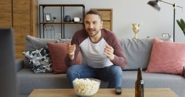 Genç erkek spor hayranı evde oturuyor ve kaybettiği için üzgün ve kızgın bir şekilde TV 'de maç izliyor. İçeride.