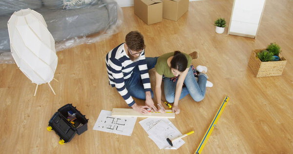 Top view of the young just married couple doing a wooden decoration for their new home while sitting on the floor in the living room. Inside