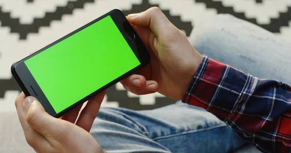 Close up of the mans hands with a green screen smart phone horizontally. Chroma key. Over shoulder