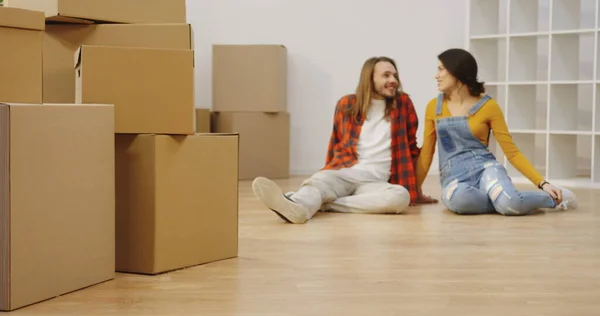 Many boxes in front of the camera and talking young couple on the blurred background in the emty flat. Young people moving in together. Indoors