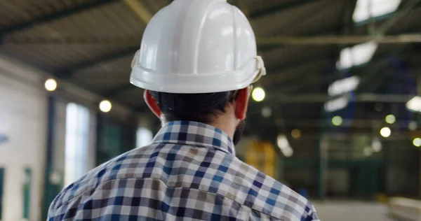 Achteraanzicht op de mannelijke werker in een geruit hemd en een helm lopend in de industriële inrichting. Sluit maar af. Binnenkant — Stockfoto