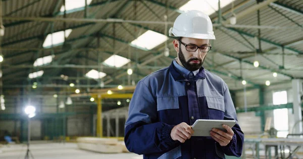 Caucasian male factory worker walking with a tablet device in his hands. Manufactory space. Indoors. Portrait