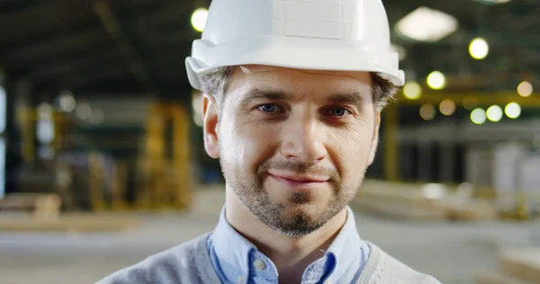 Close-up van knappe ingenieur in een helm poserend en glimlachend naar de camera in de grote fabrieksruimte. Binnen. Portret — Stockfoto
