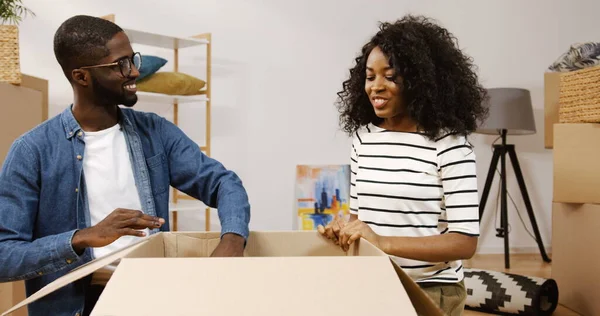 Šťastný pár Afroameričanů, který sedí s velkou krabicí a fotí z ní fotku v rámečku, dívá se na ni a směje se v místnosti plné krabic. Jdeme na to. Uvnitř Royalty Free Stock Obrázky