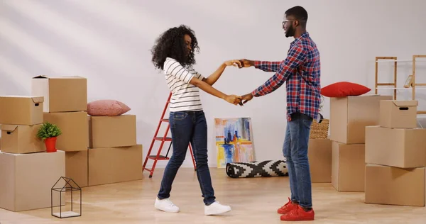 Young just married African American woman and man moving in together in their new apartment and dancing among unpacking boxes in the big living room. Indoor Stock Picture