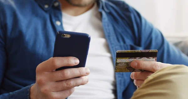Primer plano de las manos masculinas sosteniendo un teléfono inteligente e introduciendo el número de la tarjeta de crédito durante las compras en línea. De interior Imagen de archivo