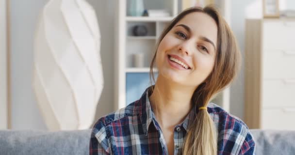 Portret van de jonge blanke vrouw in het geruite blauwe shirt die oprecht glimlacht voor de camera. Sluit maar af. Binnenshuis — Stockvideo