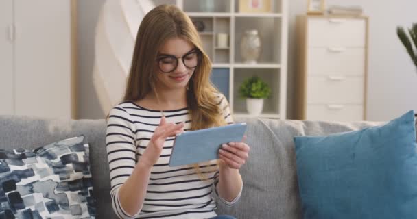 Portret van de jonge mooie vrouw zittend op de grijze bank en scrollend op de tabletcomputer in de gezellige kamer. Binnenkant — Stockvideo