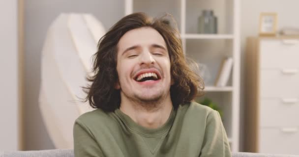 Close up of the young handsome man with a long dark hair looking at the camera and laughing loudly in the nice light room. Portrait. Inside — Stock Video