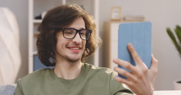 Caucásico joven hombre guapo en las gafas de tener un videochat mientras está sentado en el sofá en casa. De cerca. En interiores — Vídeos de Stock