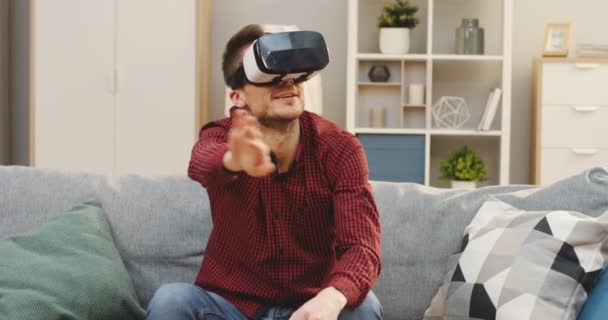 빨간 검정 셔츠를 입은 젊은 백인 남성의 초상화와 아늑 한 거실에 헤드셋이 있는 VR 안경이 찍힌 사진. 내부 — 비디오