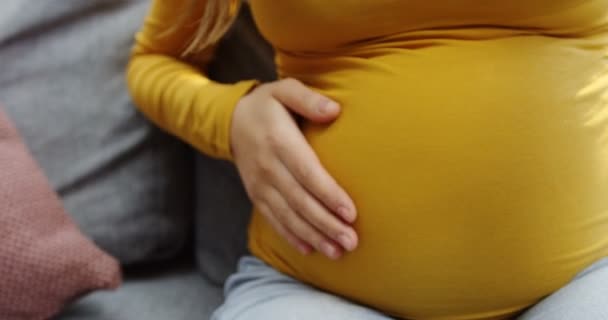 Крупный план большого беременного живота в жёлтом свитере и белой руке, гладящей его. В помещении — стоковое видео