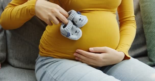 Крупним планом великий вагітний живіт і жіночі руки роблять кроки з маленькими дітьми на ньому. На сірому дивані. Внутрішні — стокове відео
