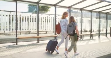 Beyaz bir annenin arkasında, otobüs durağında yürüyen, tekerlekli bavulları taşıyan ve konuşan küçük, tatlı bir kızı var. Kızıyla birlikte tren istasyonunda gezinen bir kadın. Yaz tatili. Arka plan.