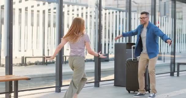 Kaukasisch glücklicher Vater und Ehemann, der von einer Reise kommt und seine Tochter und Frau im Freien umarmt. Teen niedliches kleines Mädchen läuft zu Papa und er wirbelt sie auf Händen. Hübsche Frau umarmt Mann. — Stockvideo