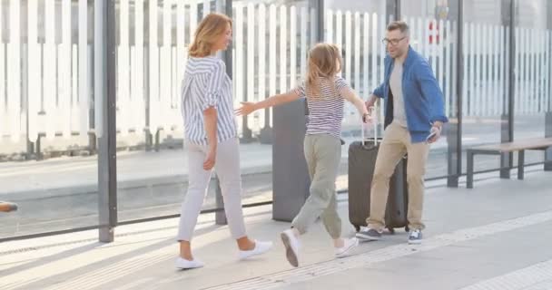 Schöner kaukasischer Mann, der von einer Reise zurückkommt und an der Bushaltestelle seine süße kleine Tochter und seine schöne Frau trifft. Kleines Mädchen und hübsche Frau treffen Vater und Ehemann nach langer Reise. — Stockvideo