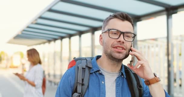 Gözlüklü, sırt çantalı, otobüs durağında duran ve cep telefonuyla konuşan beyaz tenli yakışıklı bir genç. Gözlüklü bir erkek tren istasyonunda cep telefonuyla konuşuyor. Telefon var.. — Stok video