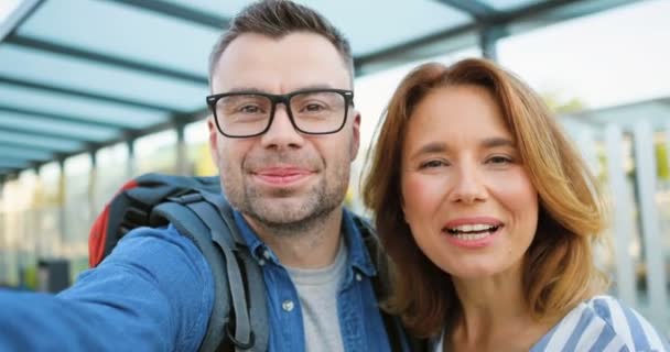 POV of Caucasian young couple of tourists standing at bus stop and talking on mobile phone via webcam. Male and female having videochat at train station. Videochatting from train station. — Stock Video