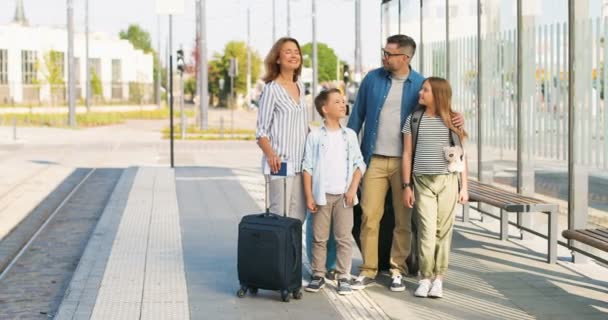 Retrato de la familia caucásica feliz con maletas de pie al aire libre en el autobús sop o estación de tren. Padres con hijo e hija viajando en verano. Vacaciones de niños con madre y padre. — Vídeo de stock