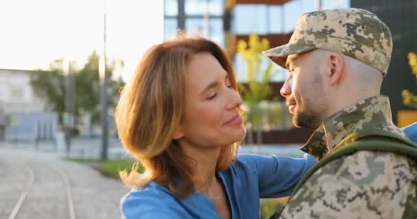 Happy young Caucasian couple talking and hugging at street with love. Handsome male soldier in uniform and hat coming back from army and meeting with beautiful wife. After long separation. — Stock Video