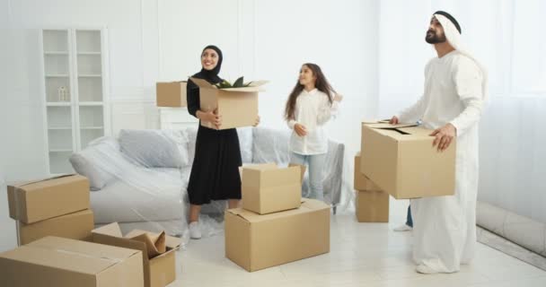 Arabian happy family with kids coming in new home and carrying carton boxes. Mother, father with kids entering house after repairment and looking around with smiles. Parents and children moving in. — Stock Video